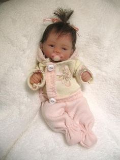 a baby doll that is laying down on a white blanket and wearing a pink outfit