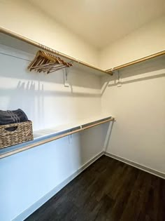 an empty walk - in closet with clothes hanging on the rails and a basket next to it