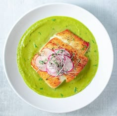 a white bowl filled with green soup and topped with grilled fish covered in radishes