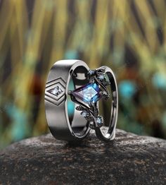 two wedding rings with blue topazte and diamonds sitting on a rock in front of some plants