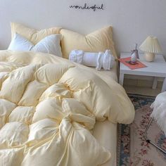 an unmade bed with pillows and blankets on it in a white room next to a table