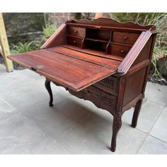 an old wooden desk sitting on top of a cement floor next to a potted plant