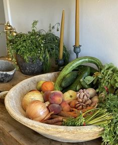 a bowl filled with lots of vegetables on top of a wooden table next to candles