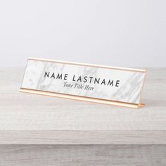 marble business name plate with rose gold trim on top of a wooden desk, next to a white wall