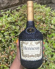 someone holding up a bottle of hennesy cogna in front of some bushes