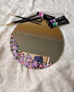 a mirror that has some paint and brushes in it on a white sheet with flowers