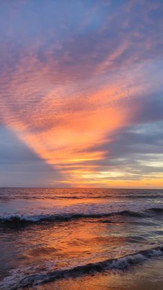 the sun is setting over the ocean with clouds in the sky and waves on the beach