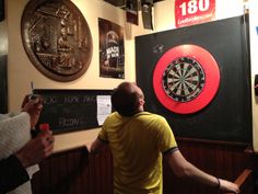 two men are standing in front of darts on the wall and pointing at them