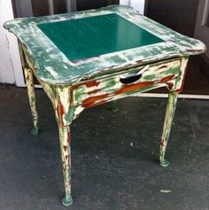 an old table with green paint on it sitting in front of a door and black shutters