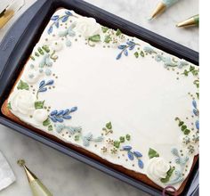 a sheet cake with frosting and blue flowers on it sitting in a baking pan