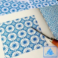 some blue and white designs are being drawn on paper with a pen next to it