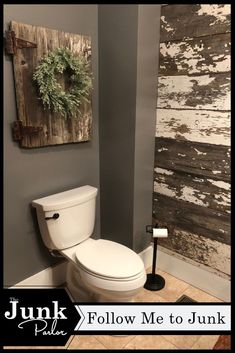 a white toilet sitting inside of a bathroom next to a wooden wall hanging on the wall