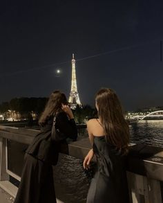 two women standing on a bridge looking at the eiffel tower