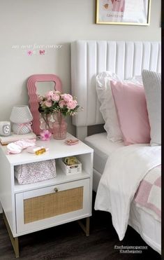 a white bed sitting next to a nightstand with flowers on top of it and pink pillows