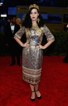 a woman in a dress and crown standing on a red carpet