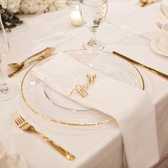 a table set with white and gold place settings, silverware, and napkins