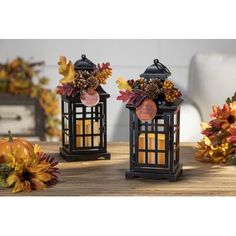 two black lanterns decorated with autumn leaves and pineconi are sitting on a table