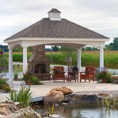 a gazebo sitting next to a small pond with chairs around it and a fire place in the middle