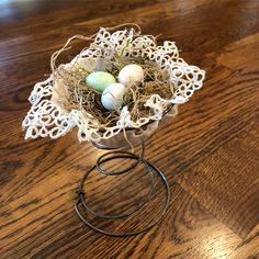 a small wire basket with eggs in it on a wooden table next to a candle holder