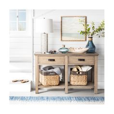 a wooden table with baskets on it next to a lamp and pictures hanging on the wall