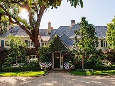 a large house with lots of trees and flowers in the front yard on a sunny day