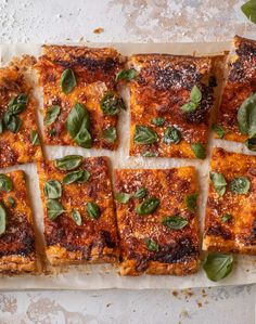 several square slices of pizza with basil leaves on top