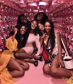 four women sitting on the floor in front of pink wall with mirrors hanging from it