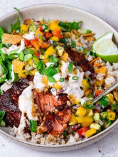 a bowl filled with rice, meat and veggies next to a lime wedge