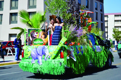 two women are riding in the back of a car decorated with grass and flowers on a city street