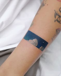 a person with a tattoo on their arm has a sky and clouds in the background