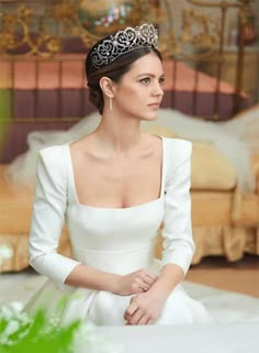 a woman in a white dress and tiara sitting on a bed with green plants