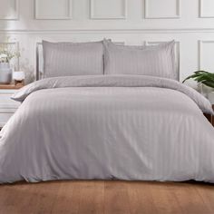 a bed with white sheets and pillows in a room next to a plant on the floor