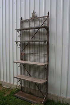 an old metal shelf with three shelves on it in front of a white corrugated wall