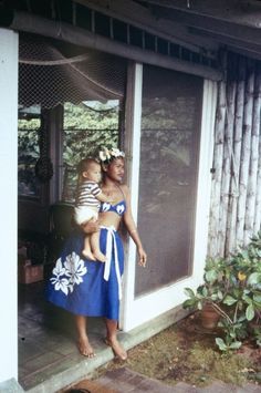 a woman holding a baby standing in front of a door with her hands on her hips