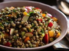 a bowl filled with vegetables and beans on top of a wooden table next to utensils