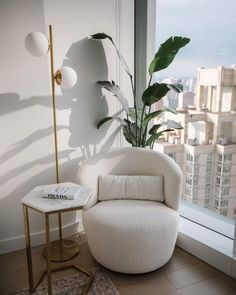 a white chair sitting in front of a window next to a table with a plant on it