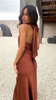 a woman in a brown dress is looking back at the camera and she has her hand on her hip