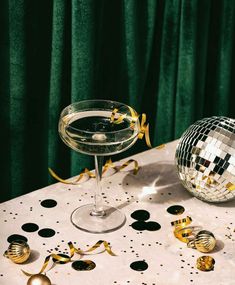 a table topped with a martini glass next to a disco ball and confetti