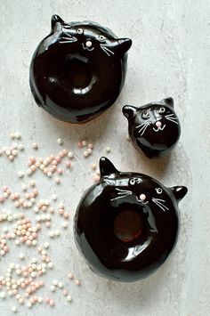 three black cat shaped doughnuts with sprinkles on the ground next to them