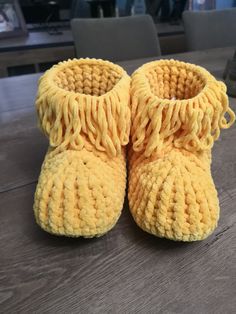 a pair of yellow crocheted baby shoes sitting on top of a wooden table