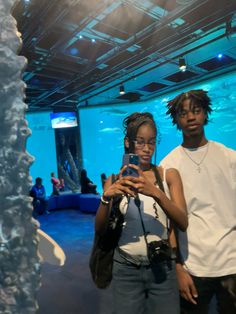 two people standing in front of an aquarium looking at a cell phone