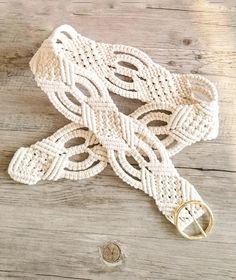 white crocheted belt with gold buckle on wooden floor next to metal button and ring