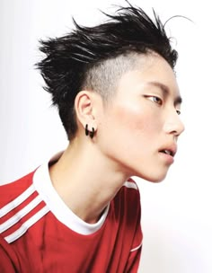 a young man with black hair and piercings on his ears wearing a red shirt