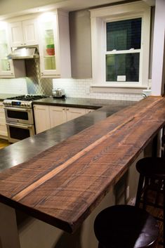 a wooden counter top in a kitchen next to two bar stools and an oven