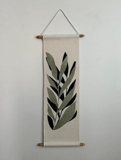 a white wall hanging with green leaves on it