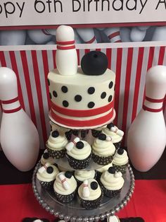 a birthday cake and cupcakes on a table with bowling pins in the background