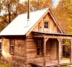 a small wooden cabin in the woods with a flag pole on it's roof