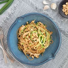 a blue plate topped with noodles and veggies on top of a gray table