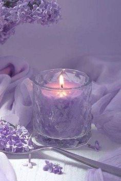 a lit candle sitting on top of a table next to purple cloths and flowers