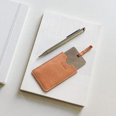 a notepad with a leather cover and a pen on it next to a notebook